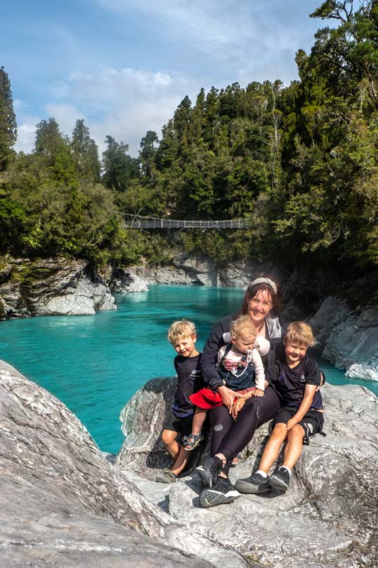 Backyard Travel Family sit on a rock at the Hokitika Gorge Walk, West Coast New Zealand