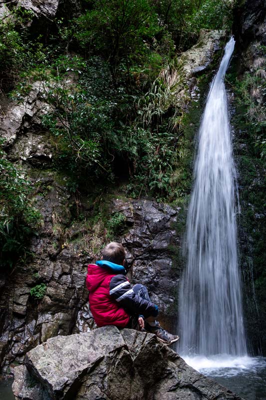 Nathan from Backyard Travel Family feels the spray on his face while sitting on a rock close to Washpen Falls, Methven, Canterbury