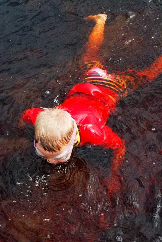 Kipton from Backyard Travel Family swims in the reddish brown, coca cola coloured lake at Lake Rotopokaka in Northland