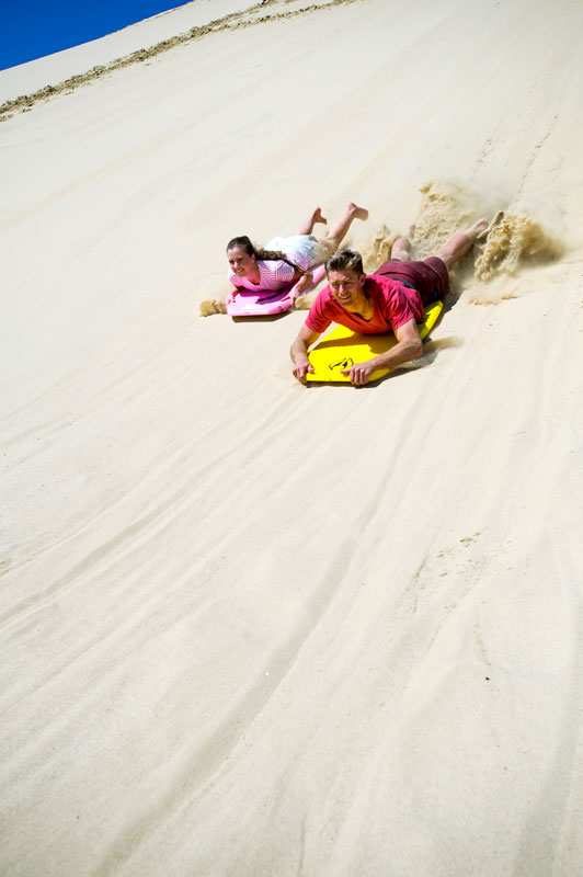Boy and Girl sandboarding down the Te Paki Sand Dunes on 90 mile beach, Cape Reinga
