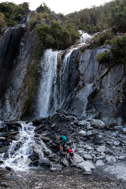 Nathan and Kipton from Backyard Travel Family explore the waterfall and drink the glacier water at Franz Josef Glacier Valley Walk