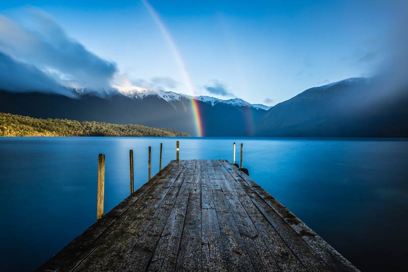 Beautiful rainbow shines over Lake Rotoiti and the wooden jetty