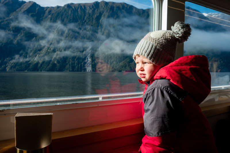 Emilia from Backyard Travel Family gazes out the window of the Milford Haven, watching the hundreds of waterfalls