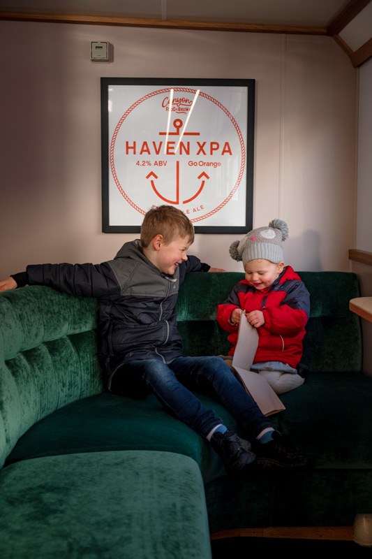 Nathan and Emilia from Backyard Travel Family sit on the green velvet couches onboard the Go Orange Haven Boat on their Milford Sound Cruise