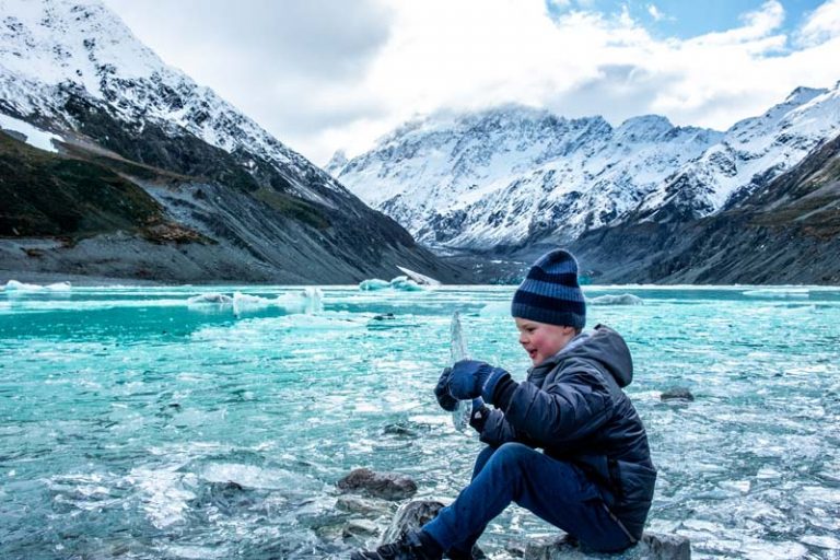 Nathan from Backyard Travel Family picks up a huge piece of ice at the Hooker Valley Track in winter