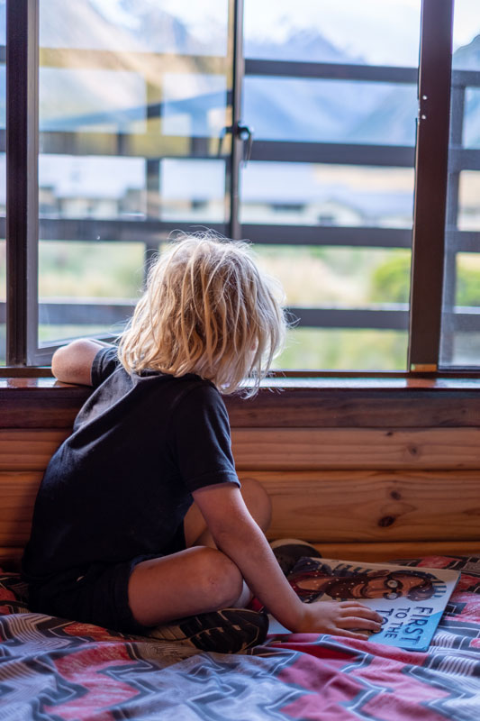 Child looking out the window of a private room at the mountains, at YHA Aoraki Mt Cook