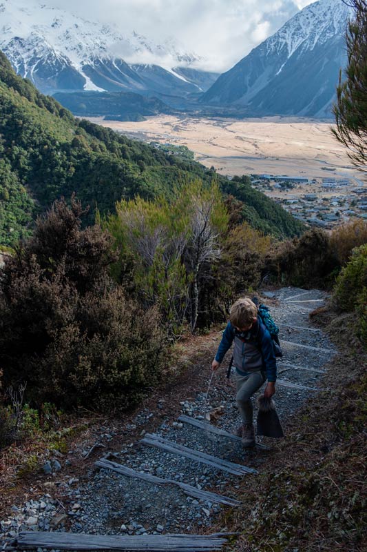 Nathan from Backyard Travel Family walks up the stairs on the Red Tarns Track, a steep uphill walk in Mt Cook, with views of Aoraki Mt Cook and Mt Cook Village