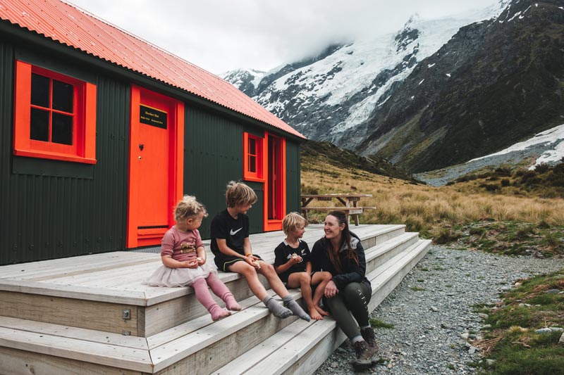 Backyard Travel Family sit in front of the Hooker Hut in Mt Cook National Park, New Zealand