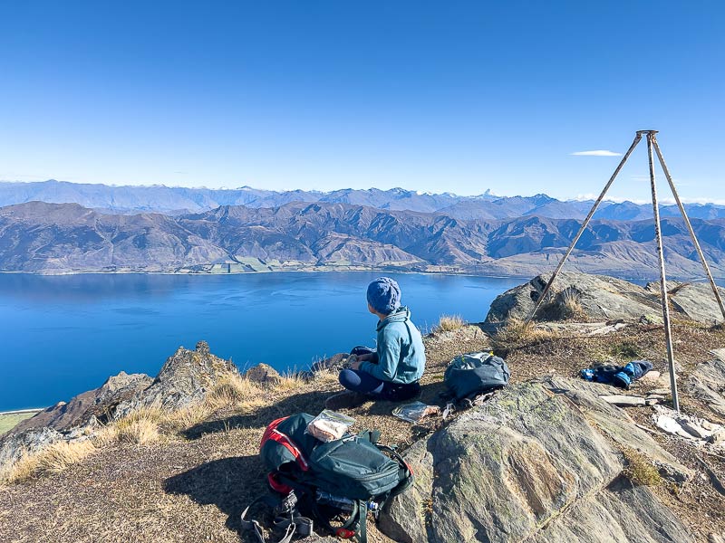 Nathan from Backyard Travel Family looks over Lake Hawea, next to the metal trig point at the Summit of the Breast Hill Track Wanaka