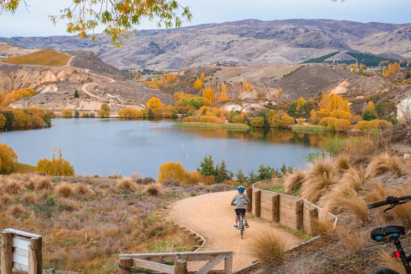 Beautiful view of a child cycling downhill from the winery on the Lake Dunstan Cycle Trail on an autumn day