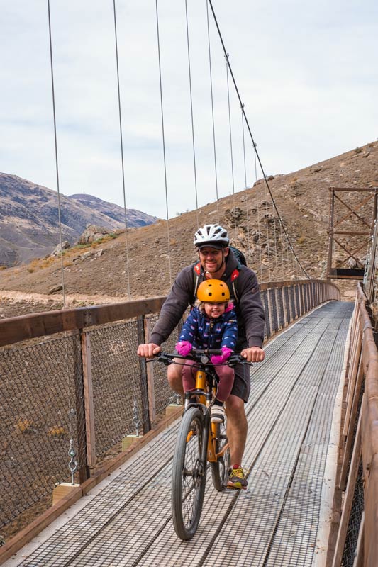 Ashley and Emilia on a kids ride shotgun seat, cross the Hugo Bridge on the Lake Dunstan Cycle Track