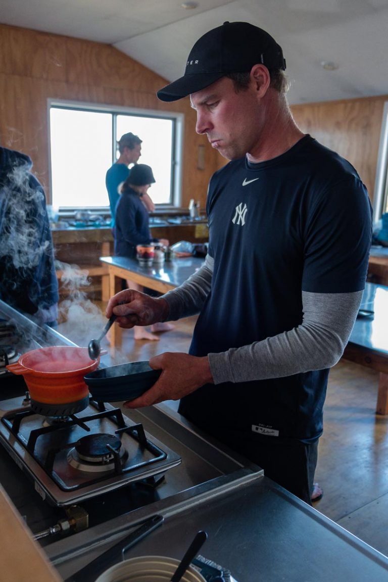 Ashley from Backyard Travel Family cooks pasta in a collapsible pot over a gas stove in the Kitchen at Luxmore Hut on the Kepler Track