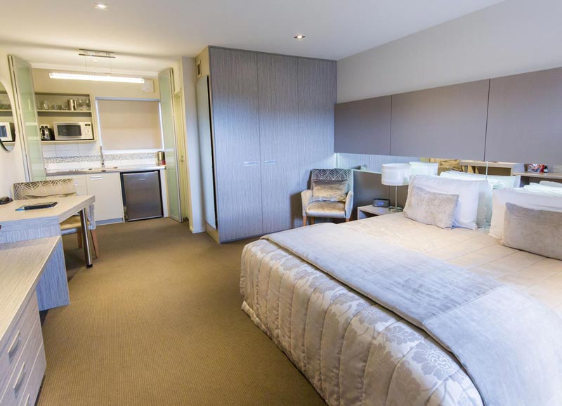 Premium suite at the Airport Gateway Motel Christchurch shows updated furnishes in blue grey neutral colours with a kitchenette at the end of the room