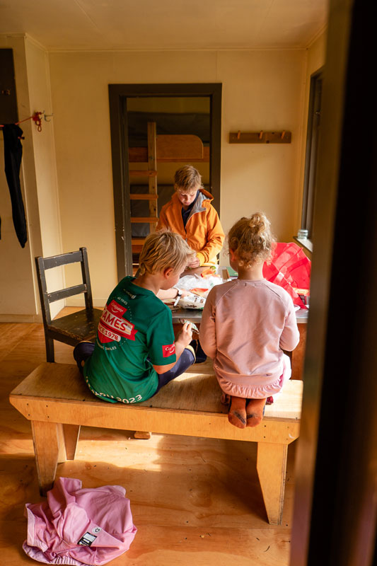 Kids sit at the wooden table while eating their lunch at Kiwi Burn Hut