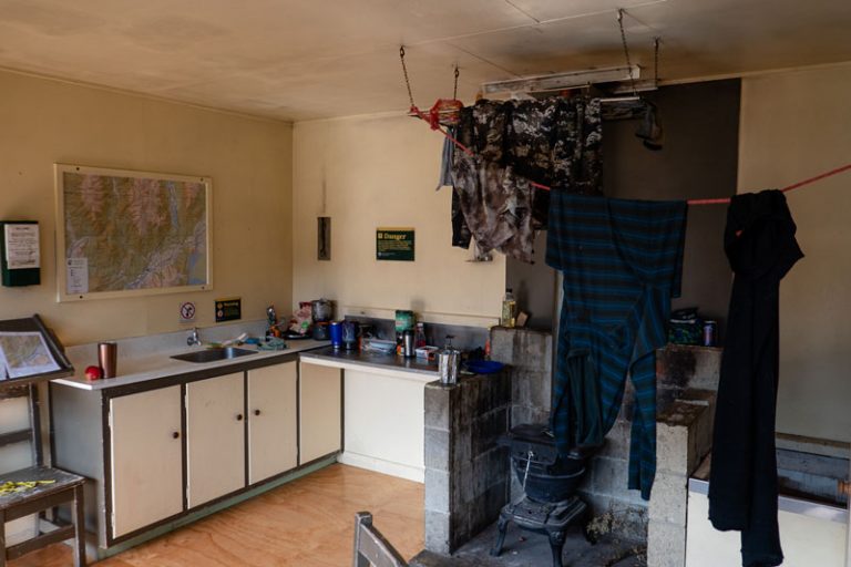 Dining and kitchen in Kiwi Burn Hut. Laundry is hanging on a rope above the log burner