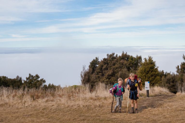 two kids walk the mt fyffe hut track with a cloud inversion layer behind them