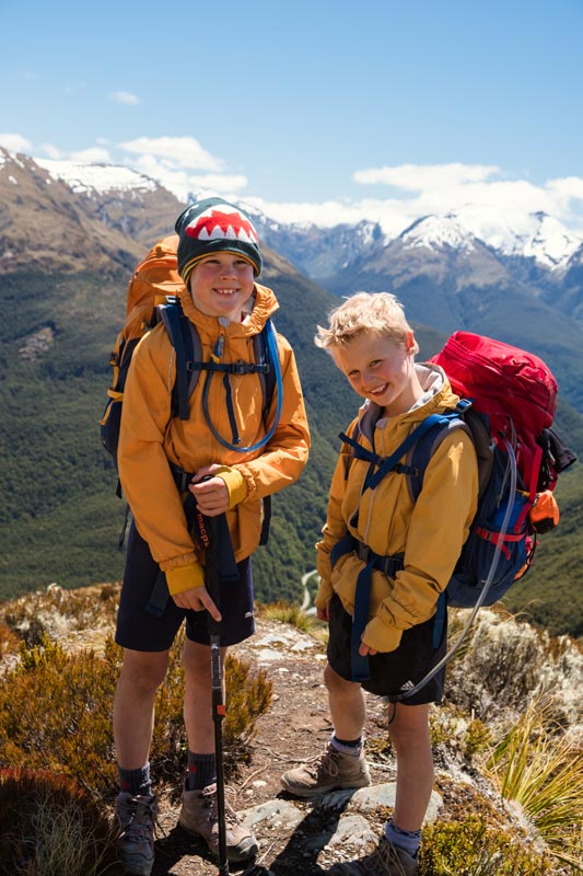 Nathan and Kipton from Backyard Travel family smile as they stand on the ridgeline of the Brewster Hut track