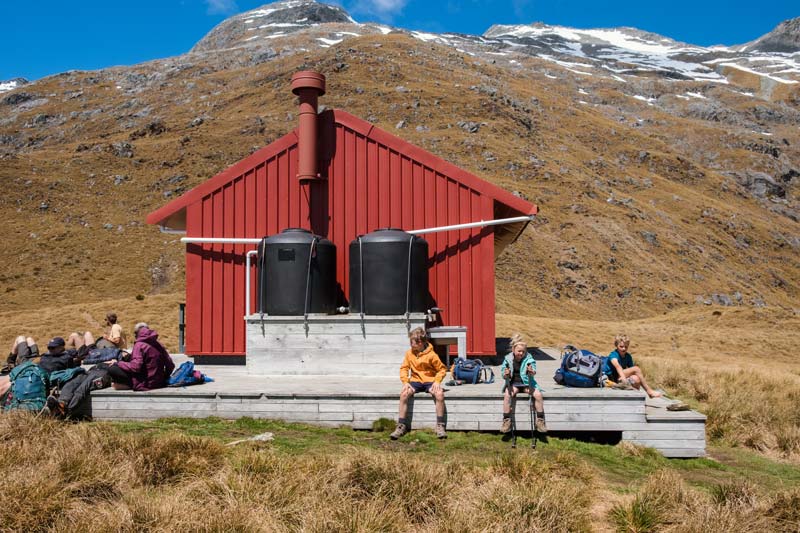 kids and fellow trampers bask in the sun on the deck at Brewster Hut