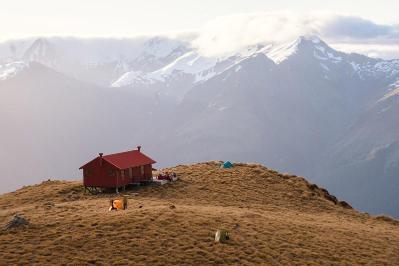 Red Brewster Hut sits on the alpine ledge as sunset with mountains set in the background