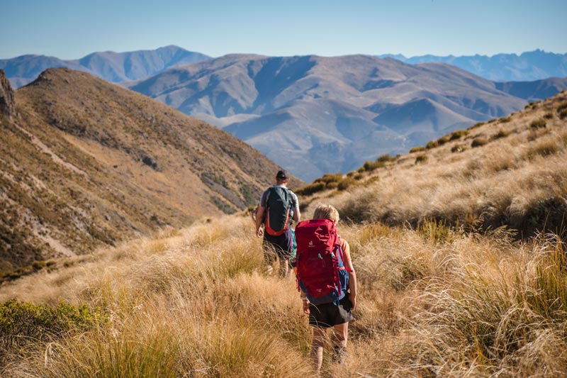 Boy with a red backpack walks with his dad downhill on the Mt Somers hike in Mid Canterbury