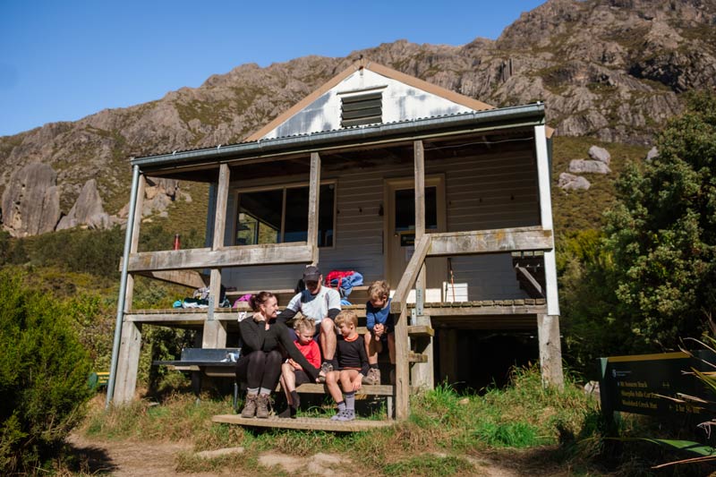 family sitting on the steps of Pinnacles Hut Mt Somers Track