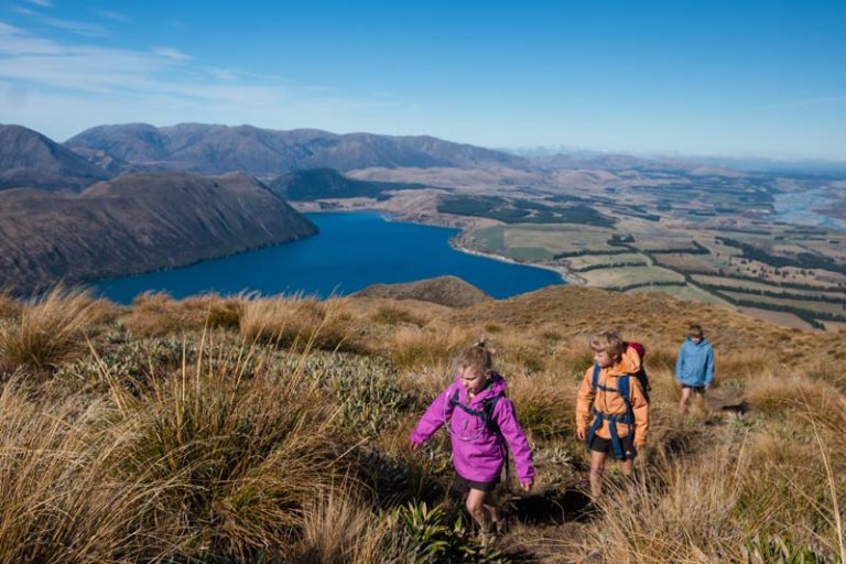 three children walking up the steep Peak Hill track with lake coleridge in the background on a beautiful Canterbury sunny day