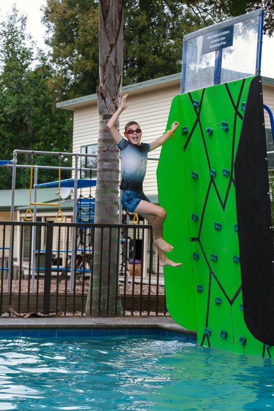 Child jumps off the rock climbing wall in to the swimming pool at the Motueka Top 10 Holiday Park