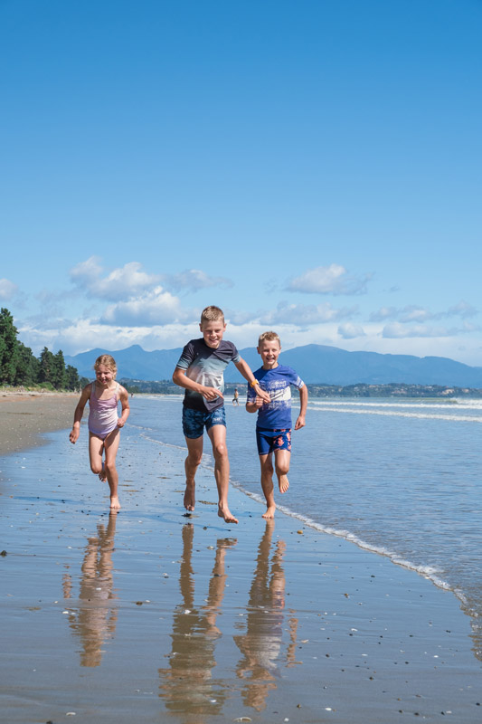 three kids run along the beach on rabbit island after cycling on the Nelson Great Taste Trail