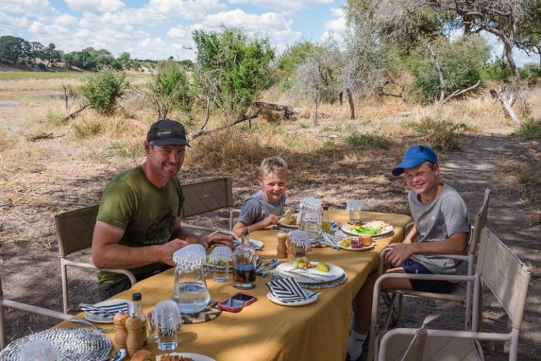 Family sit outside on the edge of the Boteti River at Moela Safari Lodge eating a suprise buffet lunch